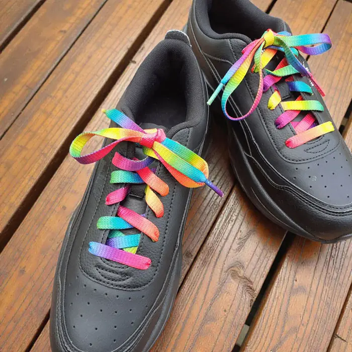 Rainbow ARASHI shoelaces in black sneakers on wooden deck