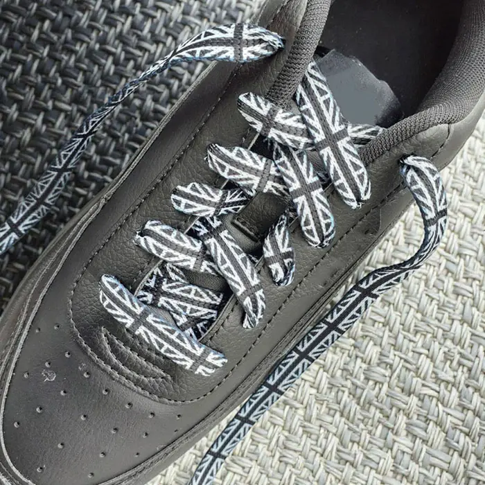 Black-and-white ARASHI Union Jack shoelaces in black sneakers on woven surface