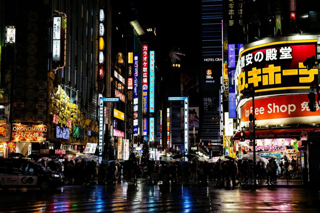 Tokyo nocą w deszczu, neonowe światła i przechodnie pod parasolami
