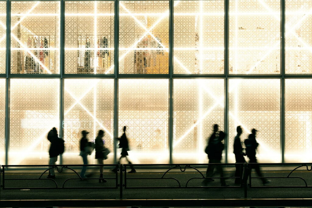 Sylwetki przechodniów na tle nowoczesnej architektury Tokio symbolizujące rytm miasta i współczesny styl życia.